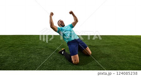 Male footballer celebrating victory, kneeling on grass, fists clenched, roaring in triumph, emotions pouring after decisive match. Male footballer celebrating victory, kneeling on grass, fists clenched, roaring in triumph, emotions pouring after decisive match. 124085238