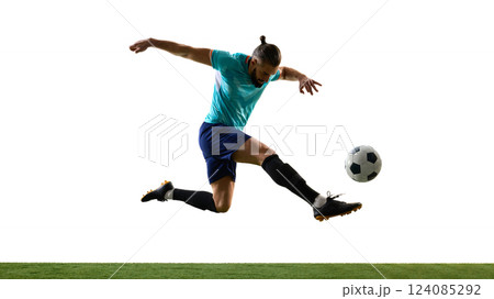 Dynamic photo of young athletic football player leaping in motion and scoring goal against white background on grassy playground. 124085292