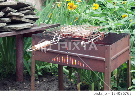 marinated beef in grill basket, cooked on red-hot charcoal in chargrill. at the tall flowering grass and bench with stones stacked on it marinated beef in grill basket, cooked on red-hot charcoal in chargrill. at the tall flowering grass and bench with stones stacked on it 124086765