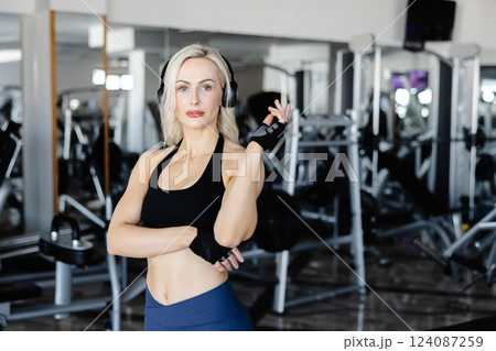 Athletic woman wearing headphones and gloves listening to music at the gym Athletic woman wearing headphones and gloves listening to music at the gym 124087259