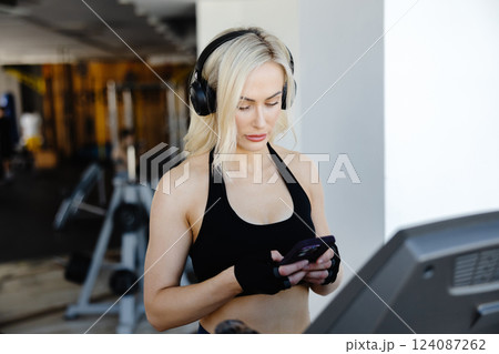 Athletic woman using smartphone and wearing headphones on treadmill in gym 124087262
