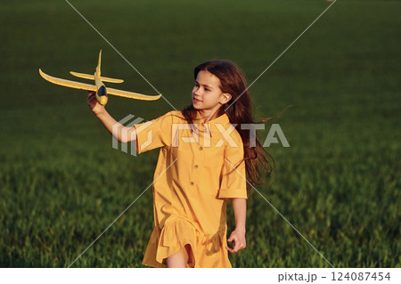 Running forward with toy plane. Happy girl have a walk outdoors on the field at summer 124087454