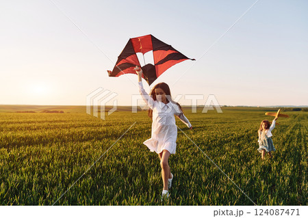 Two girls have fun outdoors on the field at summer with red kite in hand 124087471