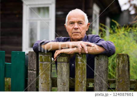 Portrait of gray-haired owner at fence of his country house in village Portrait of gray-haired owner at fence of his country house in village 124087601