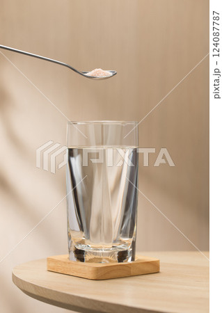 A spoon of Himalayan salt is being added to a glass of drinking water. A spoon of Himalayan salt is being added to a glass of drinking water. 124087787
