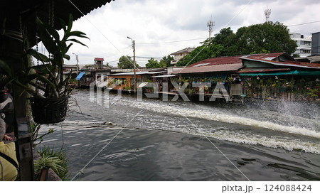 タイ・バンコク チャオプラヤ川クルーズで見る川上の古びた住宅 水上家屋とショップなのどの店と水しぶき 124088424