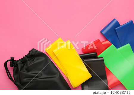A set of colorful latex rubber bands for fitness and a black cover for them on pink background. Sports concept. Space for text 124088713