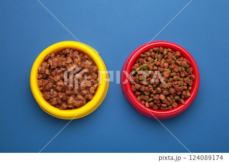 Wet and dry pet food in feeding bowls on blue background. Wet and dry pet food in feeding bowls on blue background. 124089174