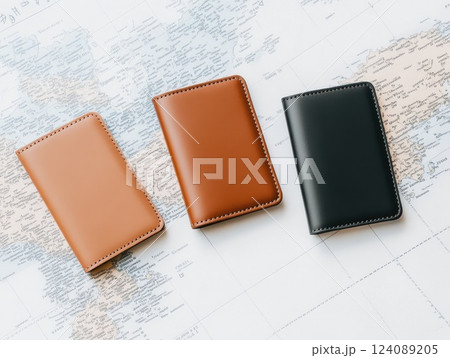 Three stylish leather wallets in different colors brown and black are neatly placed on a world map. The image highlights a professional and travel-oriented theme. 124089205