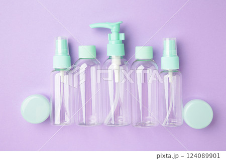 Empty travel cosmetic bottles on violet background. Minimalist bodycare beauty products for vacation or journey. Top view. Copyspace. 124089901