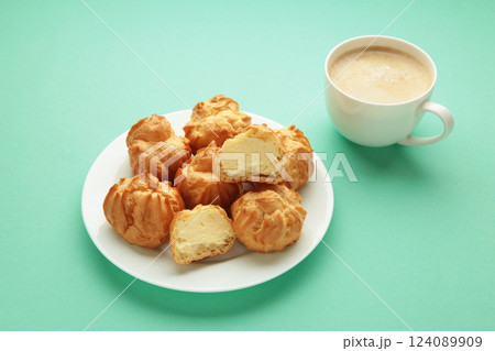 Homemade profiteroles with cream on plate with cup of coffee on mint background. Fresh baked golden profiterole. 124089909