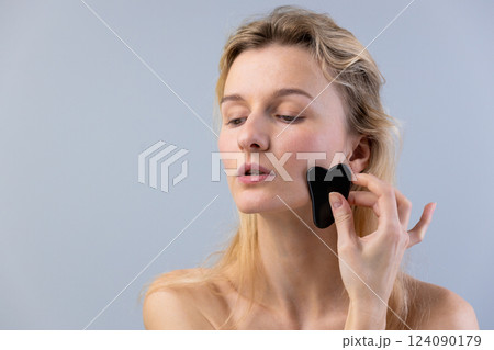 A Woman Engaging in Facial Self-Care Using a Gua Sha Tool to Enhance Skin Health and Beauty Routine for a Relaxed and Radiant Appearance in Natural Light A Woman Engaging in Facial Self-Care Using a Gua Sha Tool to Enhance Skin Health and Beauty Routine for a Relaxed and Radiant Appearance in Natural Light 124090179