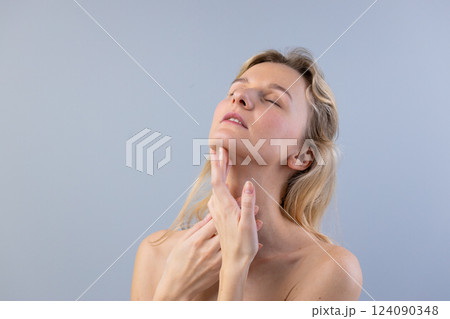 Captivating Portrait of a Young Woman with Soft Expression and Delicate Touching of Her Neck Against a Light Blue Background in a Studio Setting Captivating Portrait of a Young Woman with Soft Expression and Delicate Touching of Her Neck Against a Light Blue Background in a Studio Setting 124090348