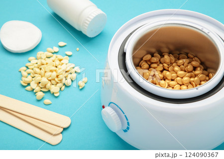 Electric wax warmer or wax heater with wax drops inside on blue background. Beauty treatments at home. Electric wax warmer or wax heater with wax drops inside on blue background. Beauty treatments at home. 124090367