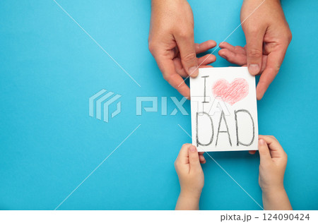 Father's Day. Child hands gives father's day greeting card to her father on blue background 124090424