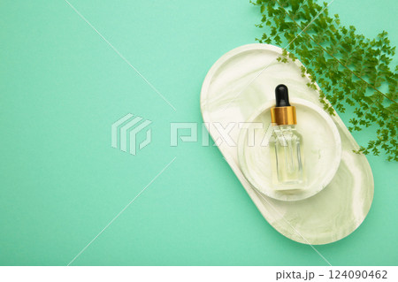 Cosmetic bottle of essential oil on plaster tray with green leaf on mint background 124090462