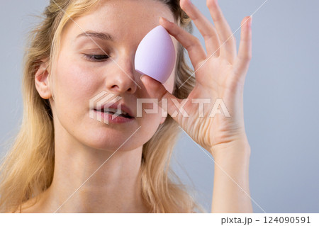 A Woman Demonstrates Makeup Application Techniques with a Purple Beauty Blender Sponge, Highlighting the Importance of Tools in Achieving Flawless Skin and Makeup Looks 124090591