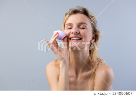 Beautiful Woman Applying Makeup with a Cosmetic Sponge, Radiating Joy and Self-Care in Soft Lighting Against a Subtle Gray Background, Promoting Flawless Skin and Confidence Beautiful Woman Applying Makeup with a Cosmetic Sponge, Radiating Joy and Self-Care in Soft Lighting Against a Subtle Gray Background, Promoting Flawless Skin and Confidence 124090607