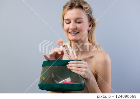 A Cheerful Woman Joyfully Displaying Her Makeup Brushes from a Stylish Transparent Cosmetic Bag Against a Soft Gray Background A Cheerful Woman Joyfully Displaying Her Makeup Brushes from a Stylish Transparent Cosmetic Bag Against a Soft Gray Background 124090669