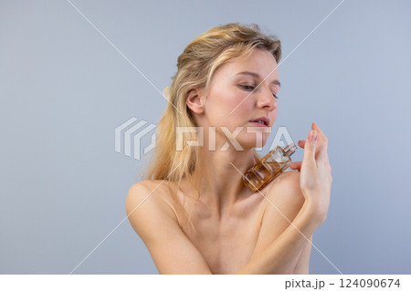Captivating Moment: A Woman Applying Perfume, Emphasizing Beauty, Elegance, and Self-Care in a Minimalist Setting with Silky Hair and Natural Make-up 124090674