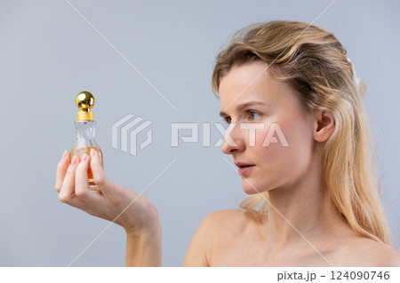 Captivating Portrait of a Woman Holding a Stylish Perfume Bottle, Exuding Elegance and Beauty Against a Soft Grey Background, Ideal for Fashion, Beauty, and Lifestyle Themes Captivating Portrait of a Woman Holding a Stylish Perfume Bottle, Exuding Elegance and Beauty Against a Soft Grey Background, Ideal for Fashion, Beauty, and Lifestyle Themes 124090746