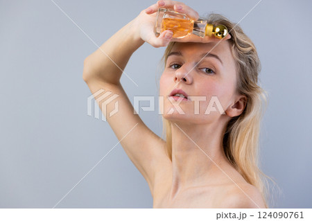 Captivating Encounter with Fragrance: A Model Elegantly Posing with a Classic Perfume Bottle Against a Soft Gray Background, Showcasing Beauty and Sensuality 124090761
