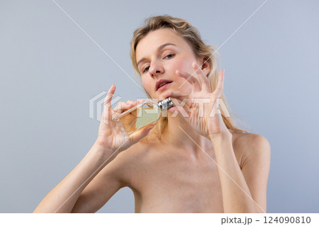 Elegant Woman Holding a Stylish Bottle of Perfume Against a Soft Gray Background, Showcasing Sophistication and Beauty in a Minimalist Setting with Subtle Lighting Elegant Woman Holding a Stylish Bottle of Perfume Against a Soft Gray Background, Showcasing Sophistication and Beauty in a Minimalist Setting with Subtle Lighting 124090810