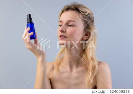 Exploring the Beauty Rituals: A Woman Carefully Examines a Blue Bottled Serum for Skin Care in a Minimalist Setting with Soft Lighting and Natural Elegance 124090838