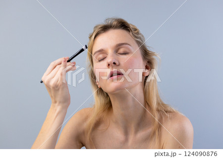 Exploring the Art of Makeup: A Woman Applying Makeup with Precision and Care to Enhance Her Natural Beauty and Confidence in a Minimalist Setting 124090876
