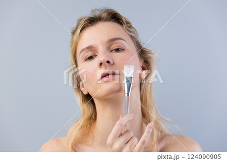 Elegant Portrait of a Woman Holding a Makeup Brush in a Studio Setting with a Soft Gray Background Emphasizing Her Natural Beauty and Makeup Application Technique Elegant Portrait of a Woman Holding a Makeup Brush in a Studio Setting with a Soft Gray Background Emphasizing Her Natural Beauty and Makeup Application Technique 124090905