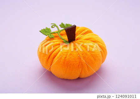 Halloween decoration toy plush pumpkin with a green leaf on purple background 124091011