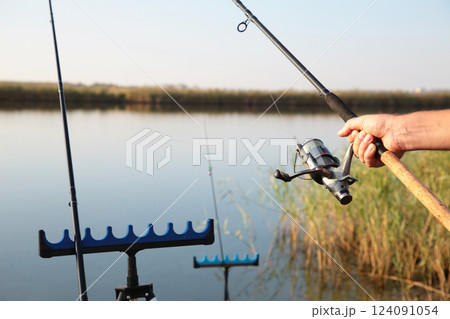 Man holding a fishing rod standing on a bridge over a river in the village where he is a regular outdoor fishing on a fun and relaxing holiday. 124091054
