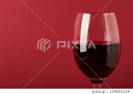 Dark studio shot of glass of red wine on dark red background. Space for text 124091254