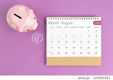August 2025 desk calendar and pink piggy bank on purple background. 124091831