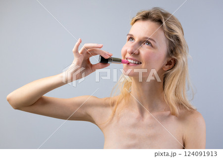 A Woman Applying Lipstick with a Playful Smile and Natural Pose Under a Soft Gray Background, Celebrating Beauty and Self-Expression with a Touch of Elegance A Woman Applying Lipstick with a Playful Smile and Natural Pose Under a Soft Gray Background, Celebrating Beauty and Self-Expression with a Touch of Elegance 124091913