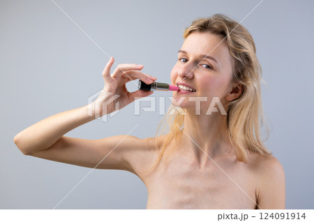 A Playful Moment Featuring a Smiling Woman Holding a Lipstick in Front of Her Lips Against a Soft Gray Background A Playful Moment Featuring a Smiling Woman Holding a Lipstick in Front of Her Lips Against a Soft Gray Background 124091914