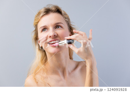 A Beautiful Young Woman Applying Soft Pink Lipstick to Enhance Her Natural Beauty, Radiating Confidence and Joy in a Minimalist Setting 124091928