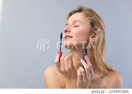 Captivating Moment: A Barefaced Woman Applying Mascara with Graceful Focus on Personal Beauty in a Calm and Serene Environment 124091966