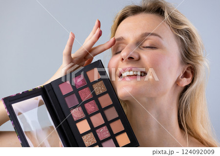 Captivating Beauty: A Woman Engaging with a Colorful Makeup Palette for Eye Shadows and Blushes, Expressing Joy and Enthusiasm in a Bright, Well-Lit Setting Captivating Beauty: A Woman Engaging with a Colorful Makeup Palette for Eye Shadows and Blushes, Expressing Joy and Enthusiasm in a Bright, Well-Lit Setting 124092009