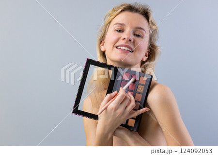 A Young Woman with Flowing Hair Shows Off a Makeup Palette While Smiling, Portraying a Vibrant Sense of Beauty and Confidence in a Stylish Portrait. 124092053