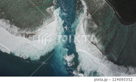 Aerial drone capturing turquoise water flowing between two white foaming waves crashing against dark reefs under a bright sun, creating a stunning tropical seascape Aerial drone capturing turquoise water flowing between two white foaming waves crashing against dark reefs under a bright sun, creating a stunning tropical seascape 124093352