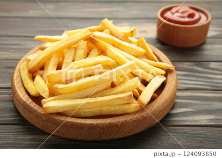 French fries with ketchup on wooden plate on brown background. French fries with ketchup on wooden plate on brown background. 124093850