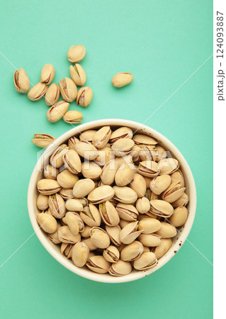 Bowl with pistachios on mint background. Vertical photo Bowl with pistachios on mint background. Vertical photo 124093887
