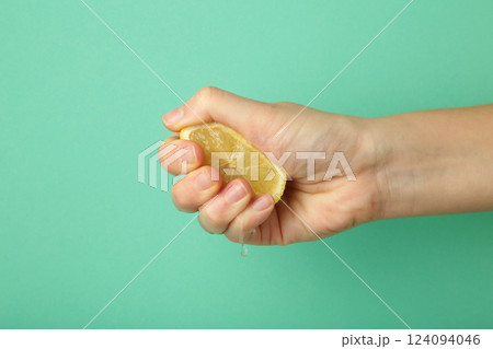 Female hand squeezing half of lemon on mint background Female hand squeezing half of lemon on mint background 124094046