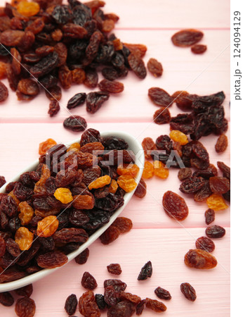 Raisins in white plate on pink wooden background. Vertical photo 124094129