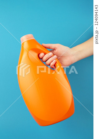 Hand with liquid laundry detergent bottle, cleaning soap for cloth on blue background. 124094143