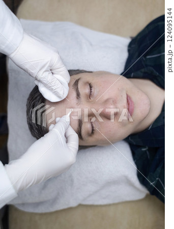 Man undergoing facial cleansing and blackhead removal. Beautician using comedone extractor or uno loop. Professional skin care in a beauty salon Man undergoing facial cleansing and blackhead removal. Beautician using comedone extractor or uno loop. Professional skin care in a beauty salon 124095144