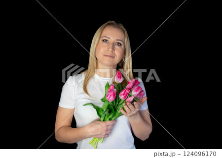 Happy blonde woman in white t-shirt holding bunch of tulips while standing against black background Happy blonde woman in white t-shirt holding bunch of tulips while standing against black background 124096170