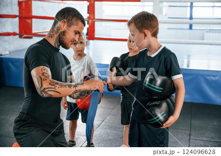 Wearing blue hand wraps. Young tattooed coach teaching the kids boxing techniques Wearing blue hand wraps. Young tattooed coach teaching the kids boxing techniques 124096628