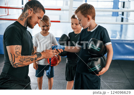 Preparing for the sparring. Young tattooed coach teaching the kids boxing techniques Preparing for the sparring. Young tattooed coach teaching the kids boxing techniques 124096629